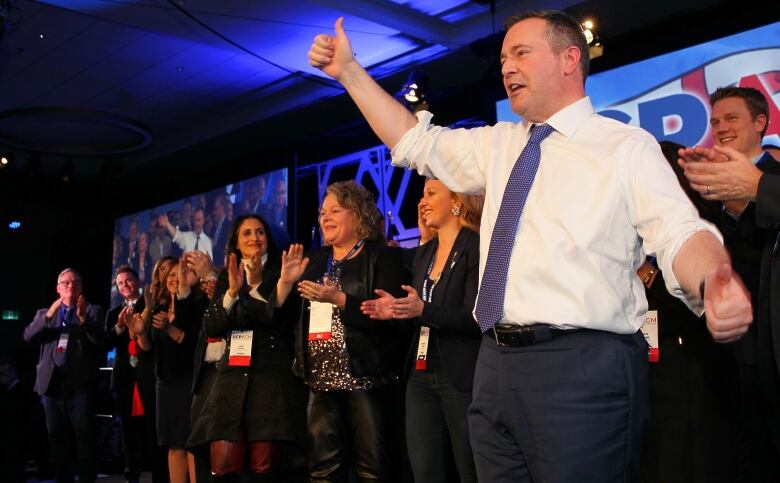 A man gives a thumbs up to a crowd. He's wearing a tie.