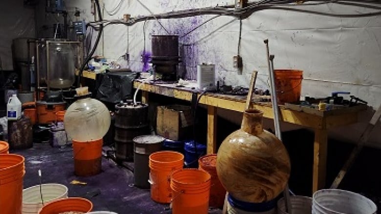 a cluttered and dirty room full of large chemistry equipment and buckets of substances