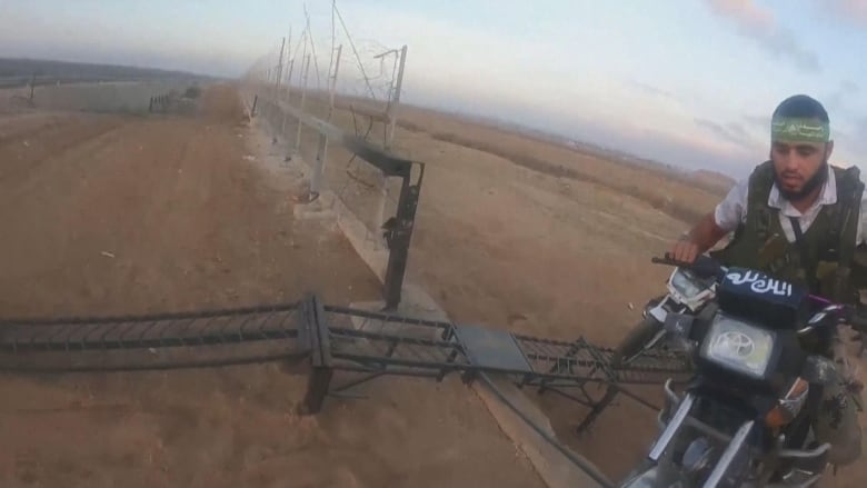 A man on a motorcycle heads through a large hole in a fence.