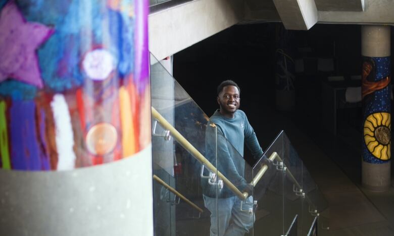 A young man smiles at the camera while standing on an interior staircase that features brightly painted pillars.