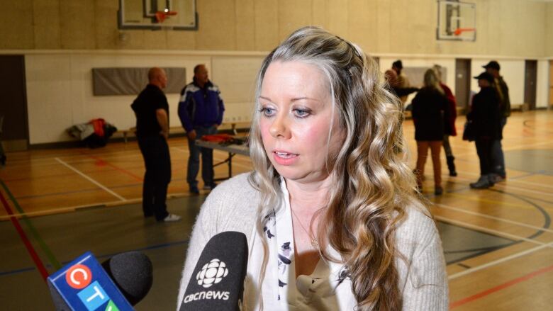 A woman in a white sweater and white shirt speaks with a pair of microphones in front of her. 