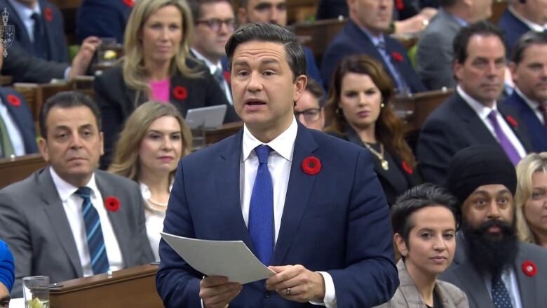 Pierre Poilievre in the House of Commons, holding a paper, wearing a poppy.