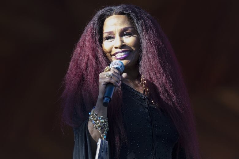 A smiling woman holds a microphone up to her mouth. 