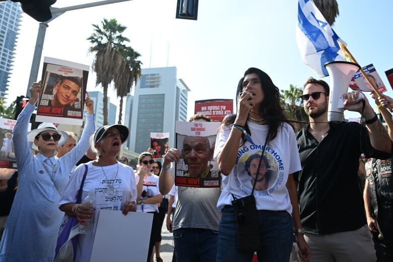 Several people, men and women, hold up signs and appear to be chanting.