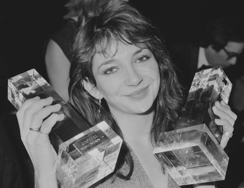 A smiling woman in black and white holds up two trophies. 