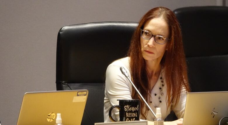 A woman with long red hair looks seriously off to the side.