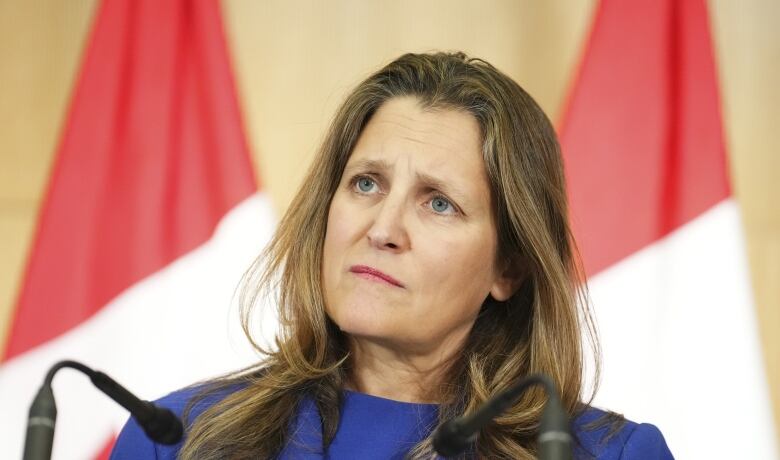 A woman stands at a podium and listens to a question from a reporter, (not shown).