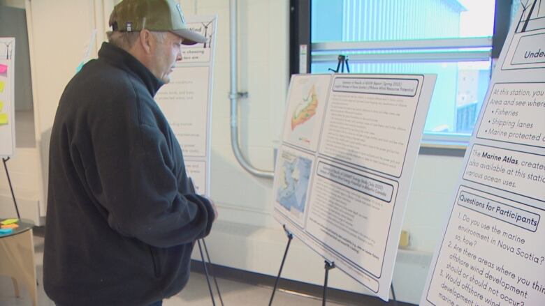 A man looks at some information panels with some text, graphics, and maps.