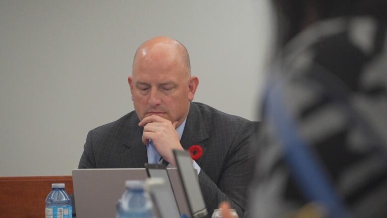 A man sits at the head of a table looking at a laptop on the desk. 