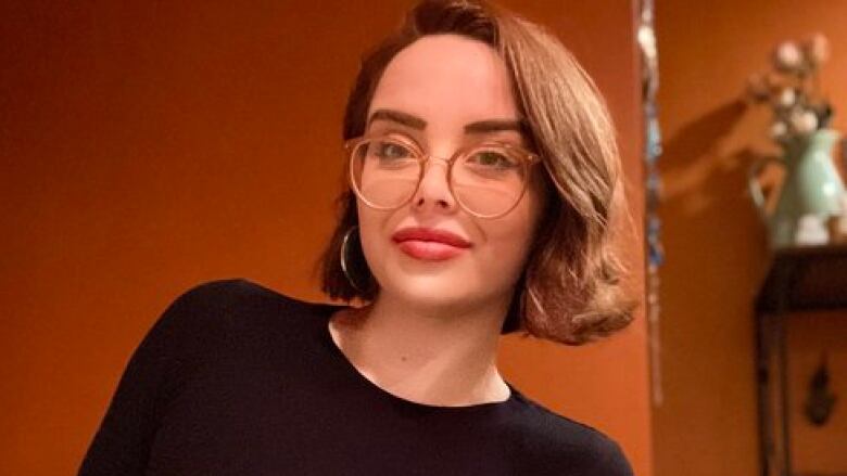 Amy Hamm, a white woman with over-sized glasses and a brown bob haircut, is show in an orange-toned photo taken from social media.