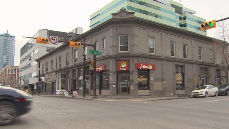 An old building sits on the corner of two streets as cars pass.