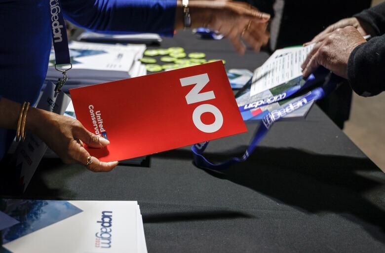 A woman's hand holds a delegate vote card that says, 'No.'