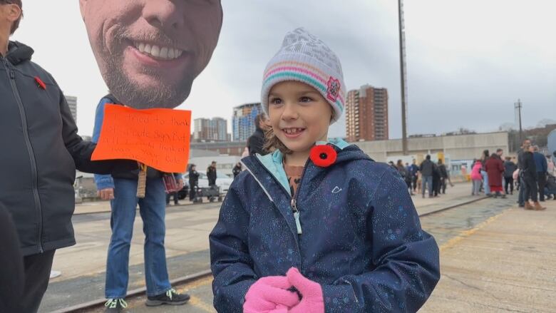 A small girl in winter clothing speaks to the camera.