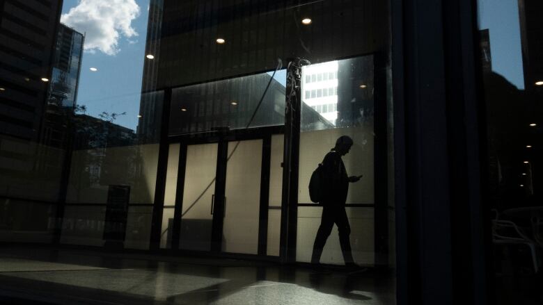 A person walks though a downtown Toronto office building with other buildings reflected in a window.