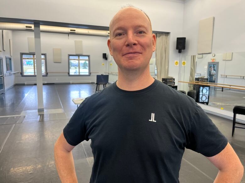 A man stands with his hands on his hips in an empty dance studio. 