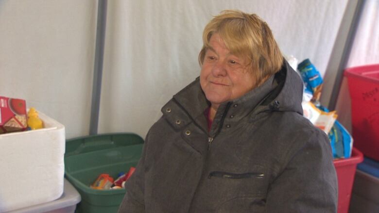 An elderly woman smiles inside a tent. 