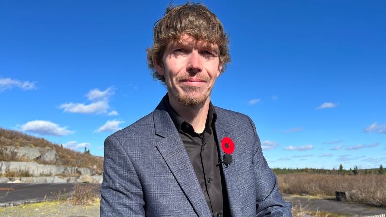 A portrait style photo of Mark Brace, dressed in a suit, wearing a poppy.