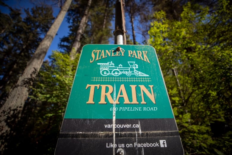 A sign reading 'Stanley Park Train' in a tree-filled park.