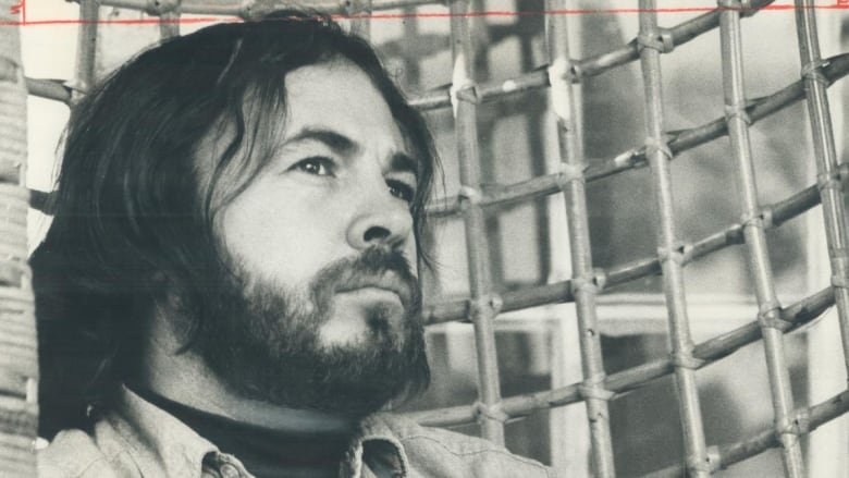 A closeup of a bearded man in a collared shirt is shown, in a sepia-toned photo that appears to be from decades ago.