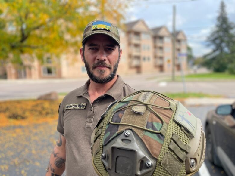 An Indigenous man holds up his Ukranian forces helmet 