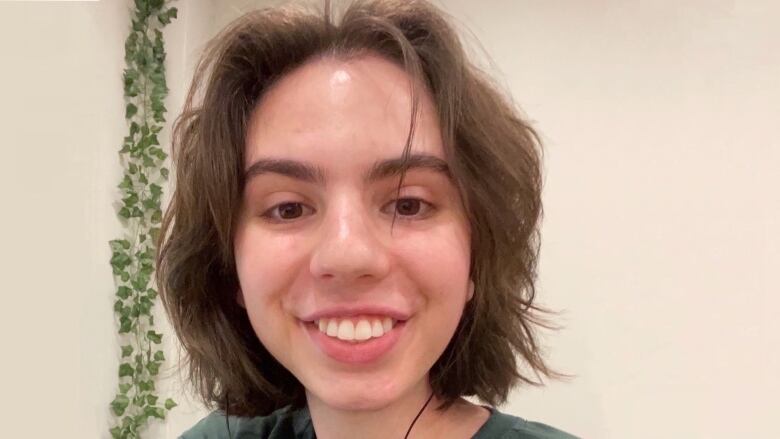 A smiling woman with shoulder-length hair standing in front of a beige wall and wearing a green t-shirt