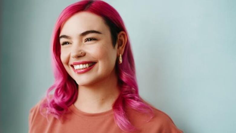 A smiling young woman with long bright pink hair and wearing an orange t-shirt