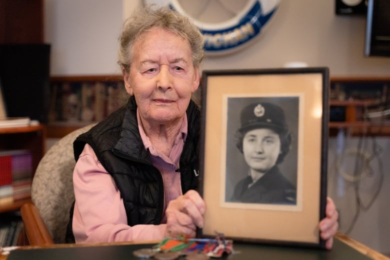 Image of Second World War veteran Betty Bell holding a black and white photo of herself when she served in the military. 