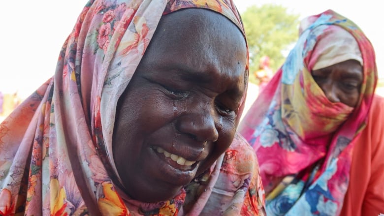 A woman with her head wrapped in a colourful scarf sobs with tears running down her face, as another woman with her face covered cries behind her.