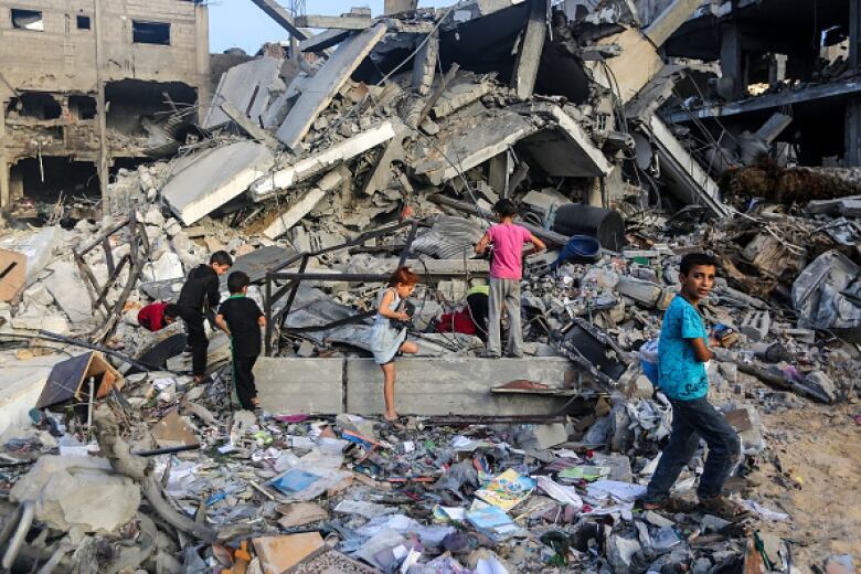 Four children plan amid destroyed buildings.