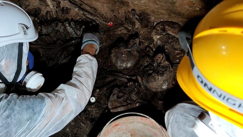 Two researchers with helmets dig among old human bones.