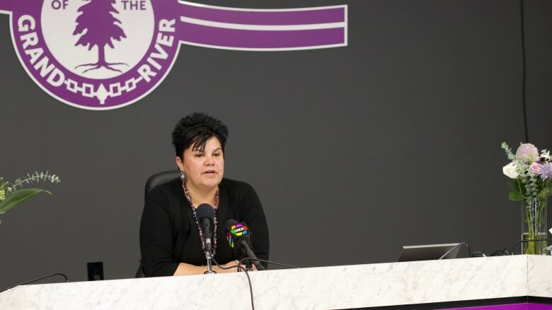 A person with short hair sits and speaks into a microphone.