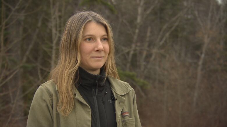 A woman with blonde hair and wearing a jacket stands in front of trees in Edmonton.