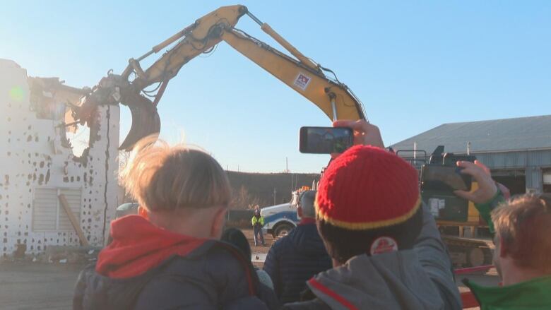 People watch as an excavator tears a building down. 