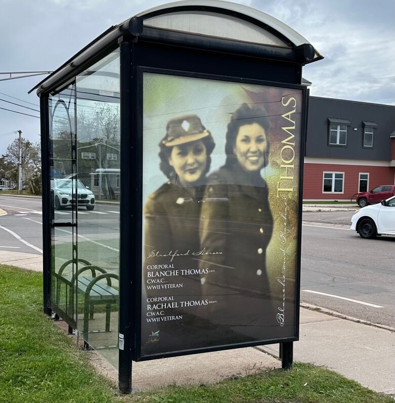 A sepia-tinted photo of two smiling young women in military uniforms is displayed as a poster on a bus shelter. 