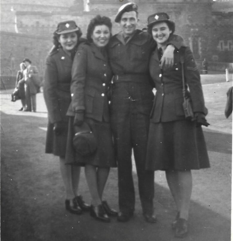 Three young women and a young man in uniform smile into the camera in a vintage photo from the 1940s. Edinburgh Castle appears in the background. 