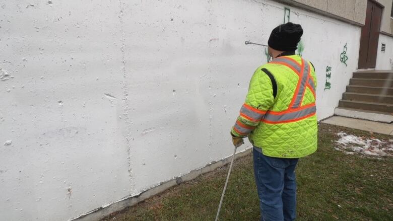 A person in a yellow reflective jacket sprays a white concrete wall.