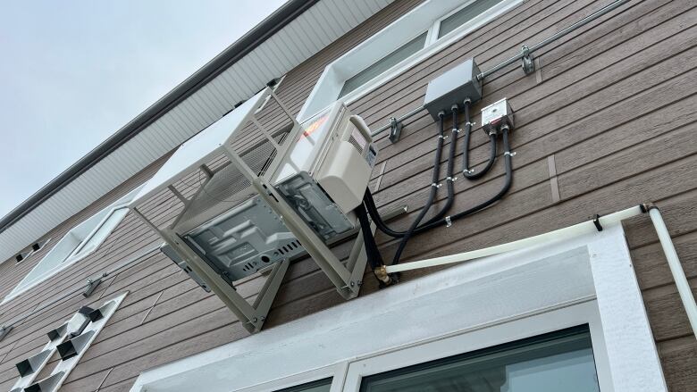 A heat pump is seen from below, mounted on the side of a building. 