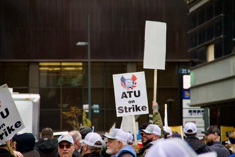 Workers group together holding picket signs. One reads 