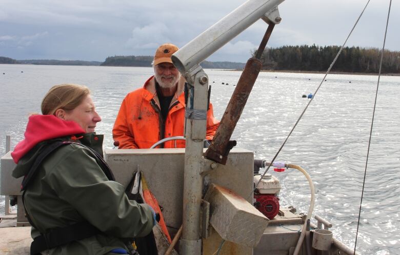 A woman and a man, wearing waterproof jackets, stand in a boat out on the water.