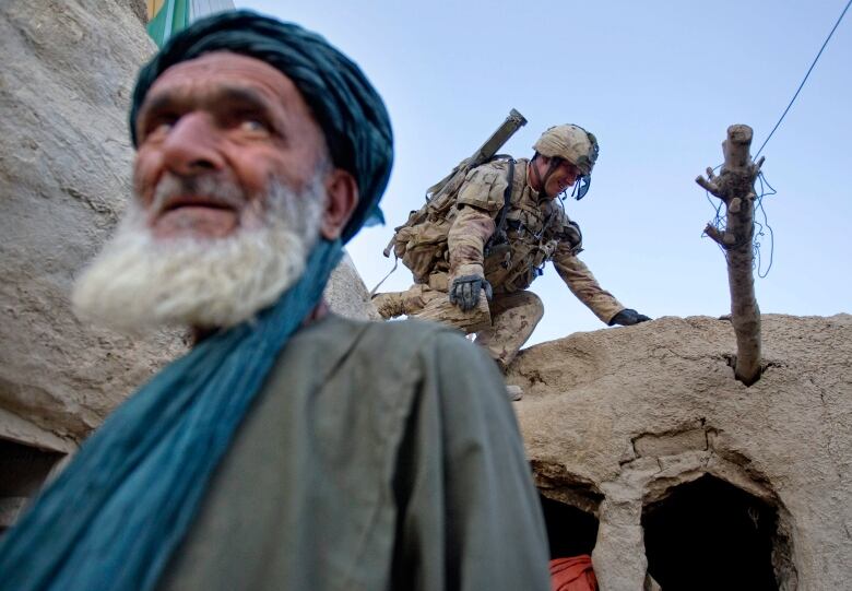 A soldier in combat kit climbs down a wall in a mud-walled compound.