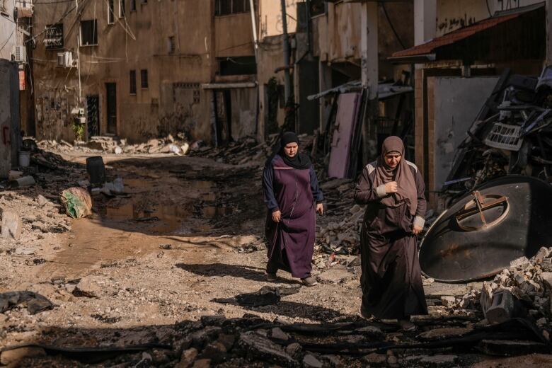 Palestinian women walk past an area damaged by raids.