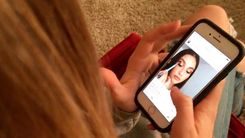 Girl watches makeup application on Instagram on a smartphone.