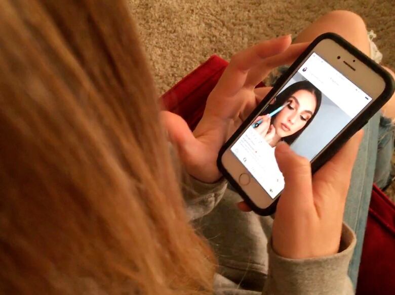 Girl watches makeup application on Instagram on a smartphone.