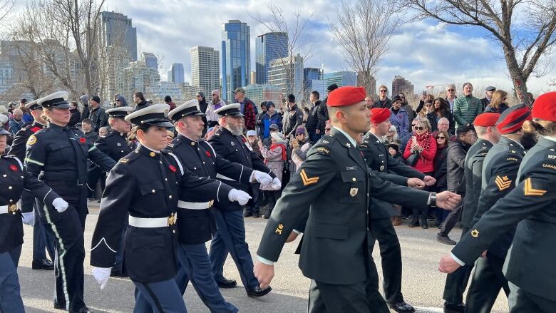 Soldiers march down a street with the Calgary skyline in the background.