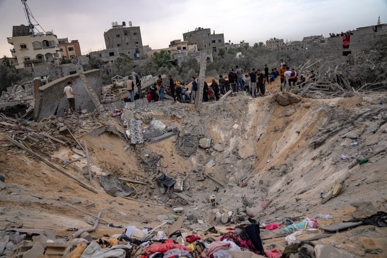 People gather around a crater filled with debris following an airstrike.