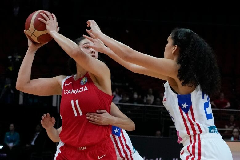 A women's basketball player looks to pass the ball past her opponent.