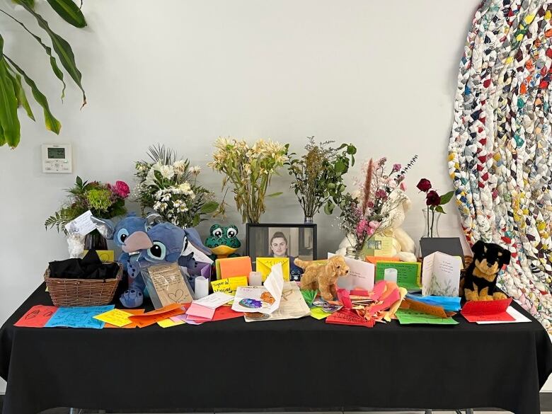 A table lined with stuffed animals, a photo and flowers. 