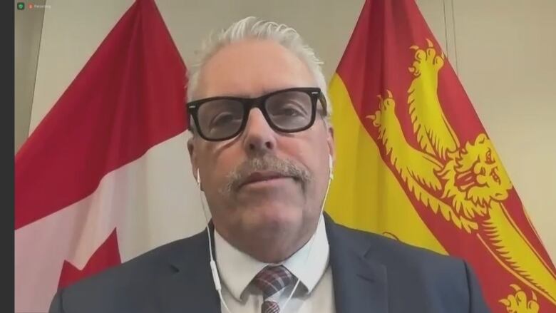 A man in a shirt and tie with dark glasses sits in front of a computer webcam.