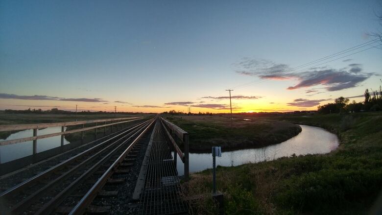 A bridge, creek and hill sit below a beautiful blue and orange sunset