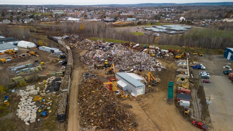 Various piles of crushed metal with a rail line and rail cars on the left side.